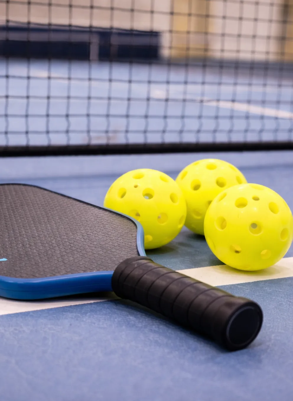 Pickleball paddle and yellow pickleballs on blue court in front of net